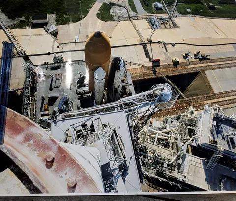 Possiblly never before seen picture atop the lightning mast looking down at the shuttle.  I am not 100% sure if it is Pad A or B.  The Masts were 60ft hight and 5ft in diameter made of fiberglass that had guide wires to the ground.  The photographer is uncredited as this was poster from a wall.