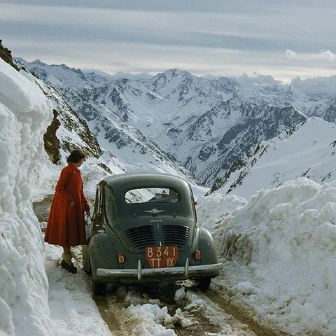 1956, a woman steps outside of her car on a snowy road in the Pyrenees, France. Photo Justin Locke.