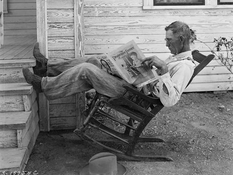 A September 1931 photo of man in Texas lounging in a rocking chair while reading