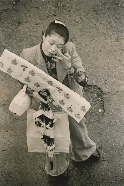 In 1974, Masahisa Fukase photographed his wife, Yōko Wanibe, every morning from the window of their apartment in Tokyo as she left for work.