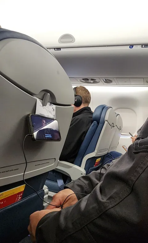 Guy on the plane put his boarding pass in his phone case, holding it up with the tray table latch