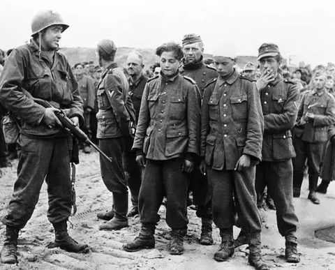 A US soldier guards a group of German prisoners of war captured on Omaha Beach: teenagers and old men. June 6, 1944.
