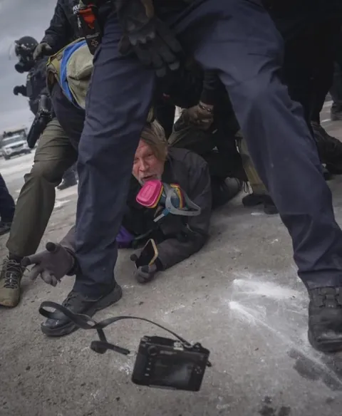 Photographer John Abernathy throws his camera to another photographer to prevent ICE from taking it