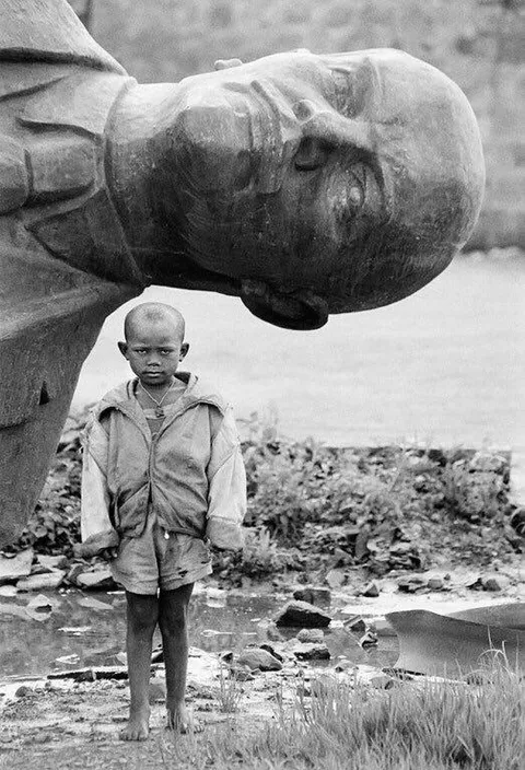 ‏a boy standing in front of a fallen statue of Vladimir Lenin in Ethiopia in 1991.