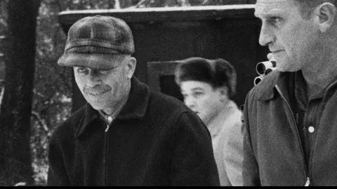 The infamous serial killer Ed Gein smiling after his arrest in 1957. Police later found furniture, masks, and clothes made from human skin inside his farmhouse.