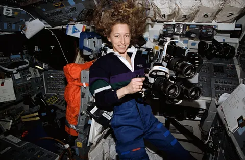 March 1994: NASA Astronaut Marsha S. Ivins "prepares to aim three Hasselblad cameras through the overhead windows of" Space Shuttle Columbia (STS-62). "The three cameras were allowed to simultaneously record the same imagery on different types of file for purposes of comparison and experimentation."