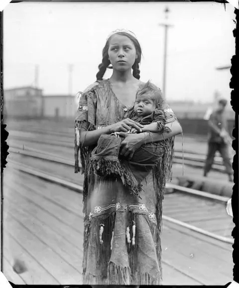 A Native American girl with a baby at a train station, 1929.