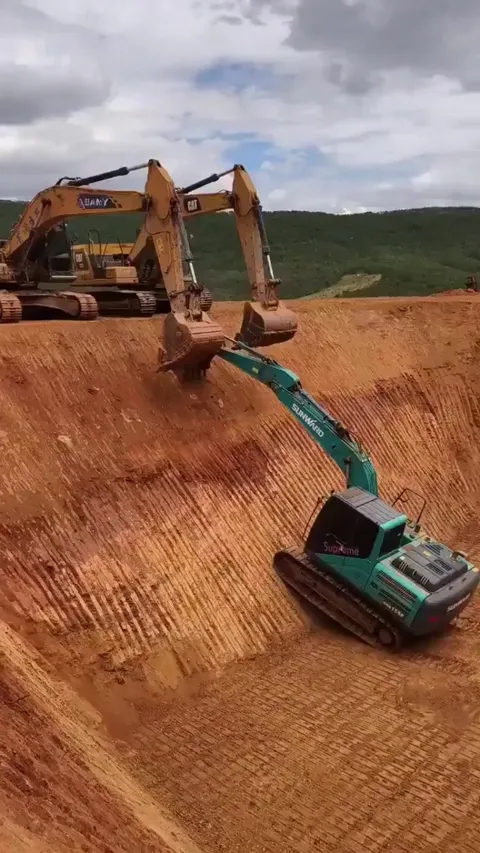 Two escavators teaming up to lift another one out of the pit.