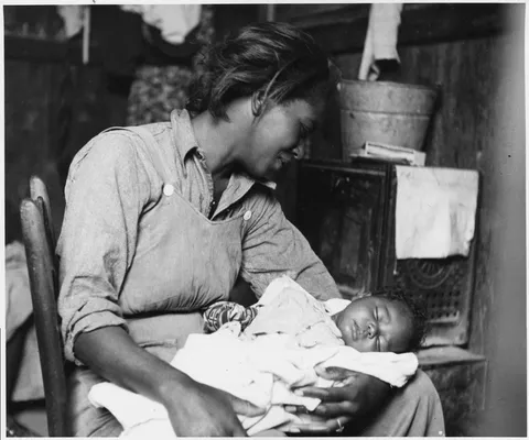 Mother gives a warm smile to her sleeping baby as they sit close to the radio, Near Buckeye, Maricopa County, Arizona, 1940.