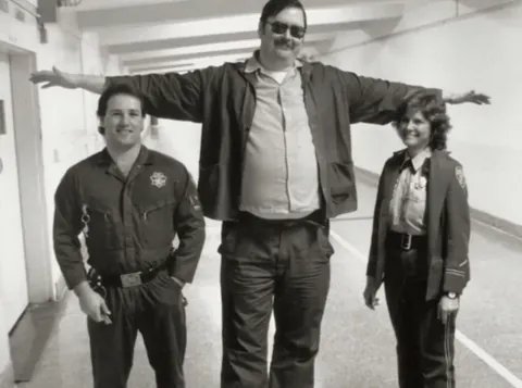 Two prison guards posing for a photo with Ed Kemper, who was 6’9 and 300lbs.