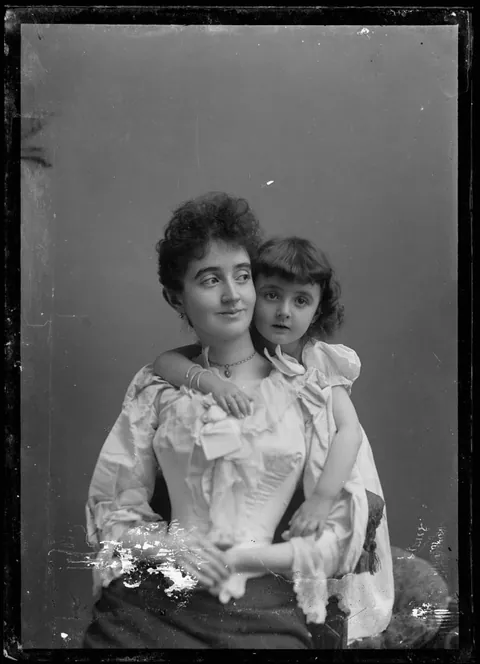 Sharp/crisp glass negative of a mother smiling while her daughter hugs her from behind, 1890s.