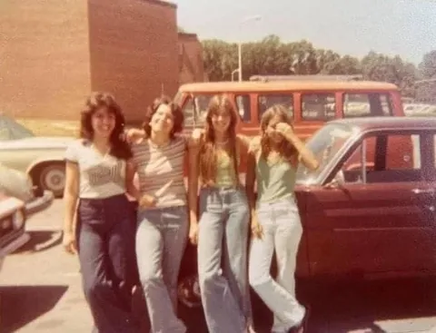 A group of young women hanging out in the school parking lot in the 1970s.