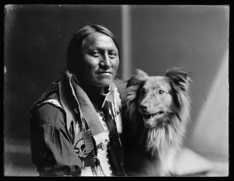 Glass negative of native Charging Thunder posing with his dog, circa (1900)