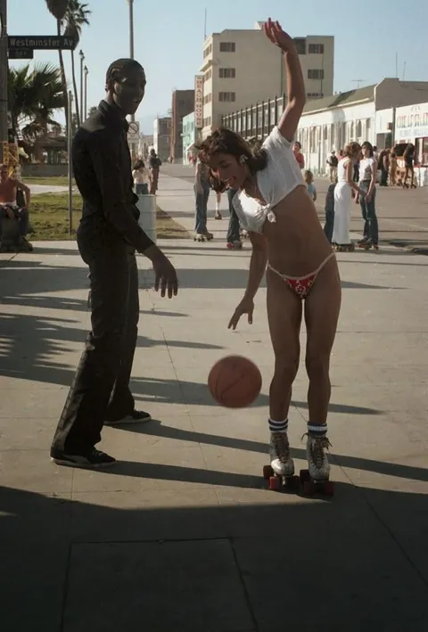 Venice Beach California during the late 1970s roller skate craze. Still has some 70s vibe but you can feel the 80s coming.