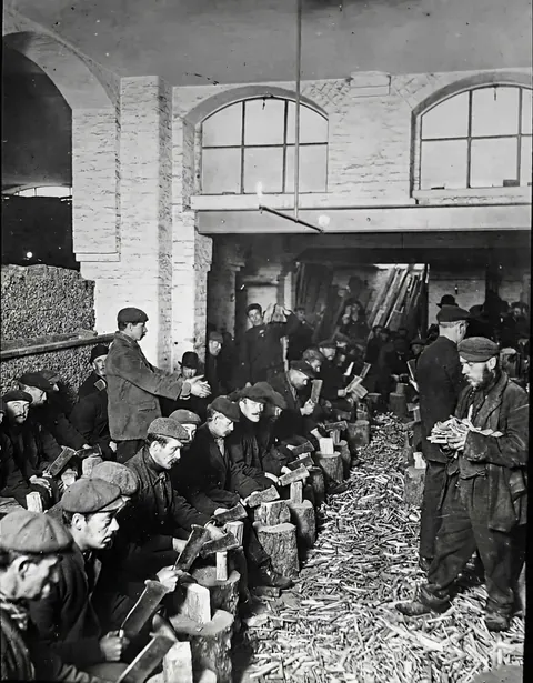 The 'Casual Ward' trap: Homeless men detained in a London workhouse, forced to chop 448 lbs of wood to pay for their night's sleep (c. 1900).