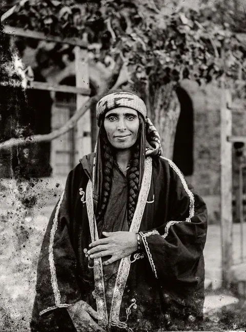 Beduin lady gives a smile to the camera in what today is Palestine. Her hair is visible in 2 thick braids. Circa 1898.