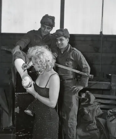Marilyn Monroe signs the cast of the leg of a soldier in Korea, 16-19 of February (1954).