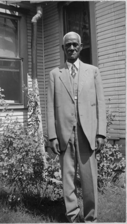 Ex'Slave Will Adams poses proudly outside his home on his sharp 3 piece suit, Marshall, Texas, 4 of December (1937)
