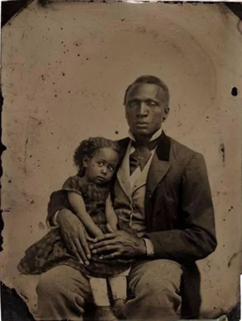 Father holds her daughter who sits on his leg for their portrait, circa 1870s. tintype.