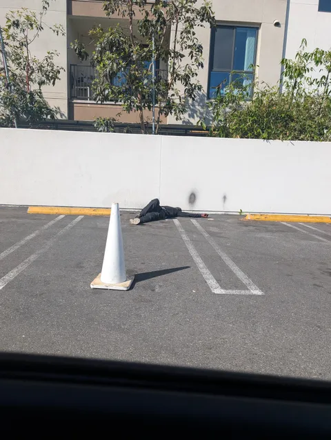 Someone put a cone to protect the sleeping homeless man in the gym parking lot