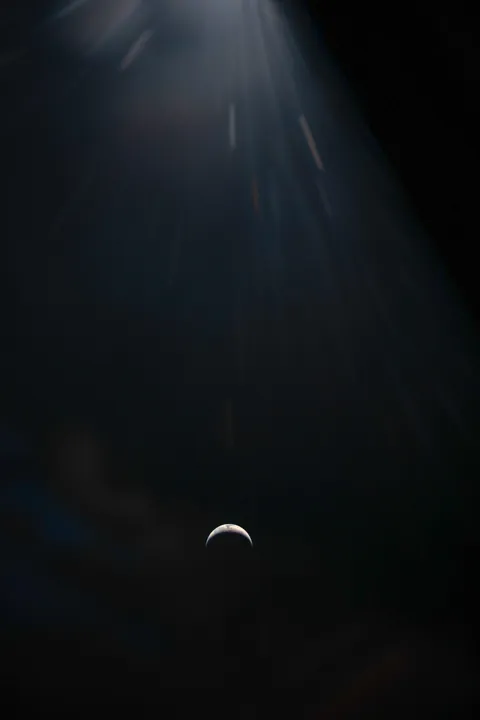 A Crescent Earth against the blackness of space is seen through the window of the Orion spacecraft.