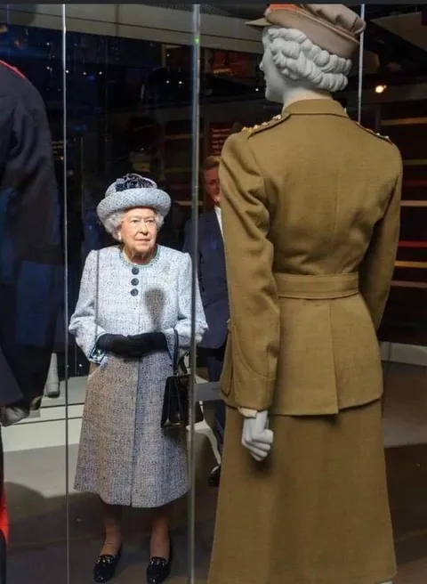 The Future Queen Elizabeth II of England, 1926-2022, a 2nd subaltern in the Women’s Auxiliary Territorial Service (ATS) stands by an ambulance in April 1945. Decades later, The Queen is photographed gazing at a mannequin wearing a uniform similar to what she wore years prior.