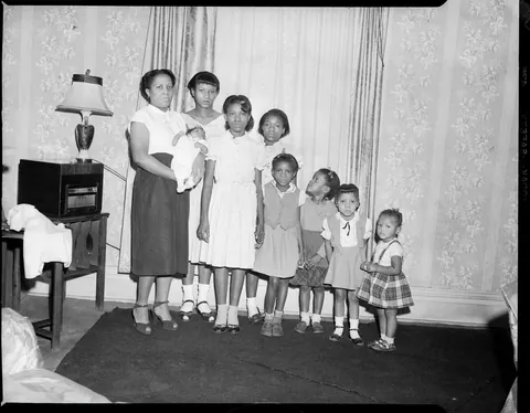 Mother smiles with her 8 children, all from oldest to youngest with the new one on her arms, circa 1950s. Safety film.