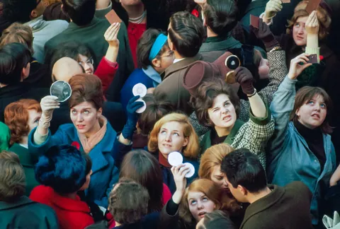 June, 1966:  Women use compact mirrors in packed crowd to catch sight of the queen in London, England.