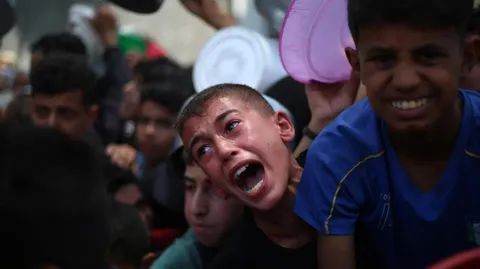 Palestinian children wait for food at a distribution point in Nuseirat, in the central Gaza Strip
