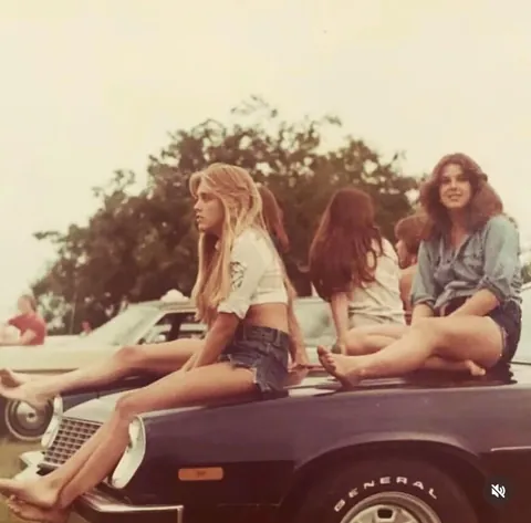 Young women sitting on the hood of a Camaro in the 1970s
