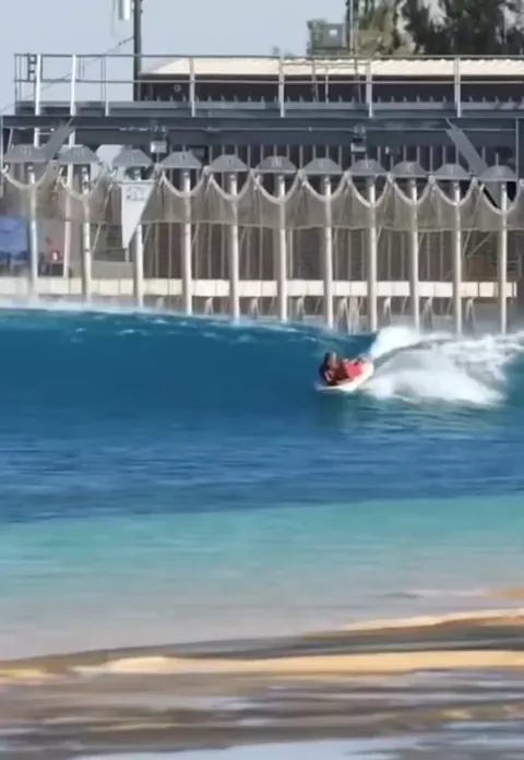 Surfing instructor teaches student all while kneeling on his own surfboard.
