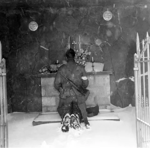 Cpl. Charles S. McNulty, of 2075 Beaver Ave., Cedar Rapids, Iowa, stops for a moment of prayer before joining his division near Houmont during the Battle of the Bulge, Belgium. 8 January, (1945)