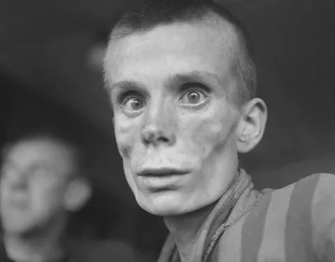 An emaciated 18-year-old Russian girl looks into the camera lens during the liberation of Dachau concentration camp in 1945