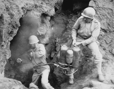 One month after D-Day, two soldiers in the 147th Infantry use a flamethrower to clear a tunnel position on Iwo Jima; hundreds of Japanese soldiers remained underground after the Marines withdrew (1945)