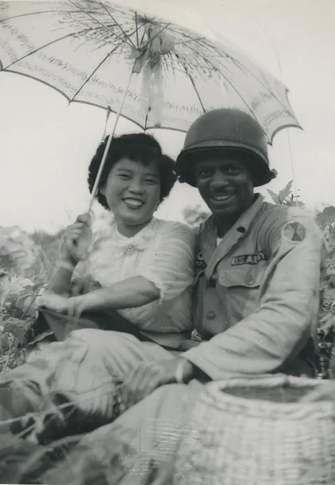 Young couple smiles and poses over a grassy hill in Korea, 1955-7.