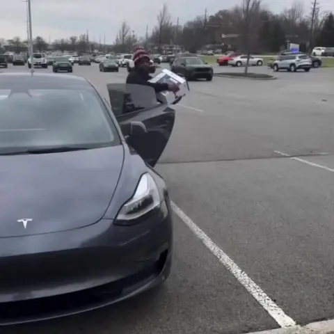 A couple giving a PS5 to a young man playing the trumpet on the street, hoping to raise enough money for one