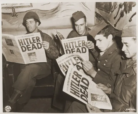 American soldiers reading about Hitler's death in the newspaper. The title alone takes up half a page.