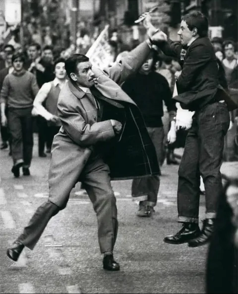 A dapper looking undercover detective disarms a man with a razor who attacked protest marchers during an Irish solidarity parade, Glasgow, Scotland, 1971
