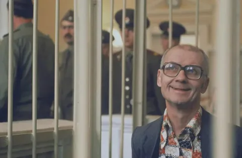 Soviet serial killer Andrei Chikatilo smiling during his trial. He was kept in his cage to protect him from the enraged relatives of his victims. 1992.