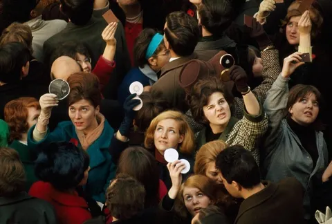 Women use compact mirrors in packed crowd to catch sight of the queen in London, June 1966.