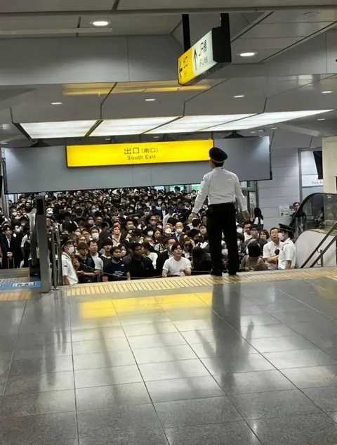 PsBattle: A large gathering of crowd in a Japanese train station with a security guard standing above them