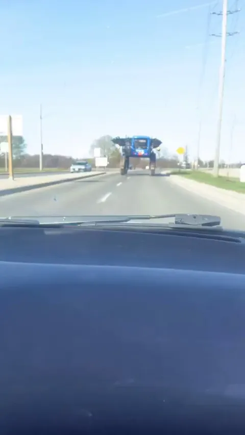 Man drives under a $600,000 New Holland crop sprayer driving down the road