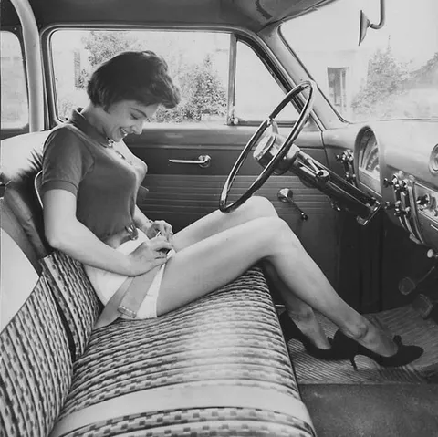 Woman inspecting this new thing, the security belt in her car, circa 1950s.