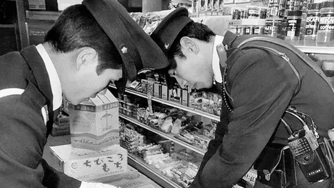 In 1984, the Fox Eyed Man calmly walked into a store, unaware a security camera was watching. Soon after, poisoned candy was discovered. Despite having his face on camera, he was never identified. The investigation consumed everyone—including a police chief who died by suicide.