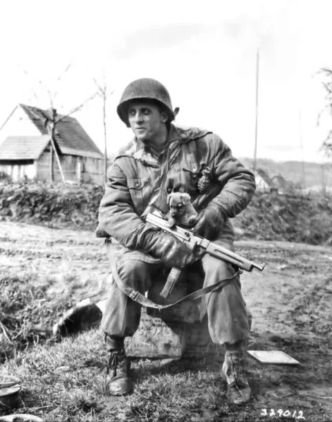 In April of 1945, paratrooper Harry Lorenzo of the 509th Parachute Infantry Battalion clutches his Thompson submachine gun and his puppy “Kaput” near Katharinenberg, Germany. (1945)