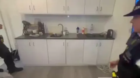 Bodycam footage by the Met Police (London) shows a secret passageway under the kitchen sink hiding £30'000 worth of illegal goods. The discovery was made during a joint operation with Greenwich Police targeting the sale of illegal tobacco and vape products.