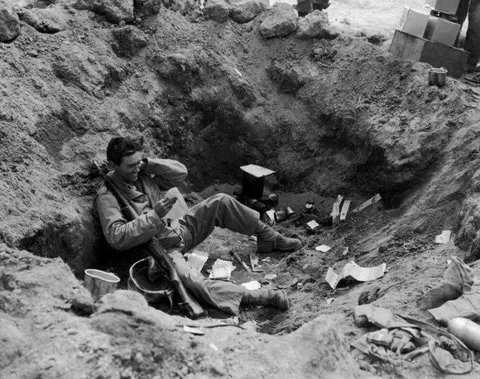 A Marine smiles while reading mail in a foxhole on Iwo Jima, 1945