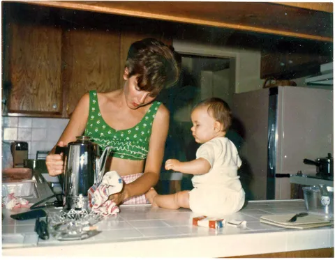 Mom cleans a spill from the coffe maker while baby sits on the counter, 1 of September 1960, kodachrome shot.