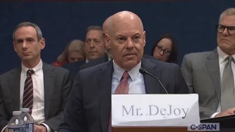 Postmaster General Louis DeJoy covering his ears during a congressional hearing