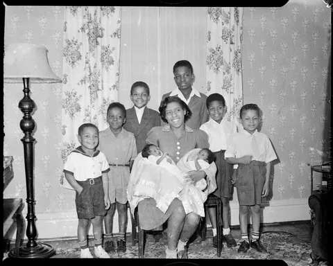 Mother gives a bright smile surrounded by her 6 children en the new twins. Agfa safety film, circa 1940s.